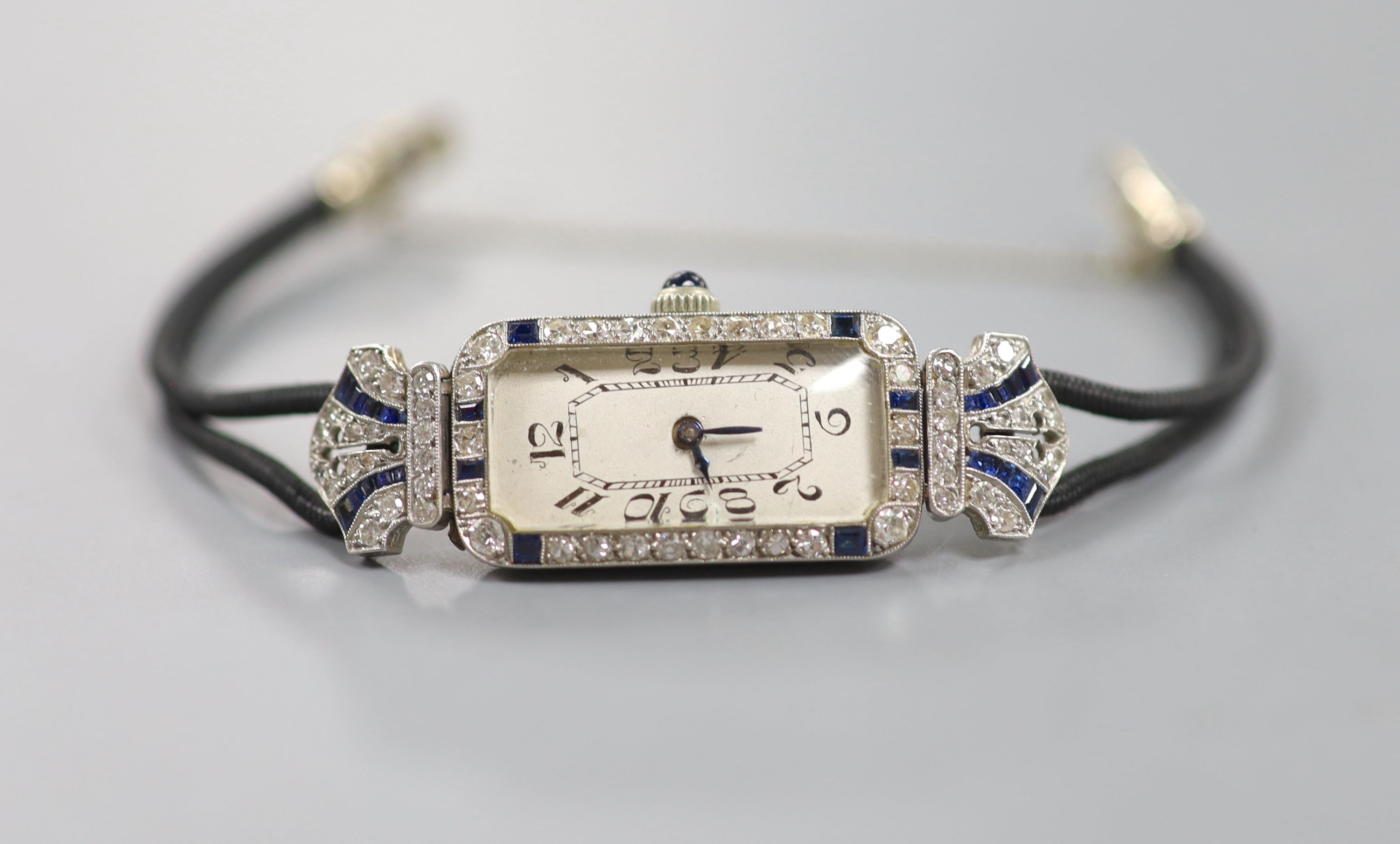 A lady's 1920's/1930's yellow and white metal, synthetic? sapphire and diamond set cocktail watch, now with battery operated movement, on a twin strand fabric strap, case diameter 15mm, gross weight 17.3 grams.